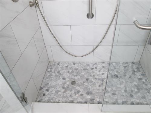 Elegant walk-in shower featuring stone mosaic floor and sleek tile design — blending comfort, safety, and modern craftsmanship.