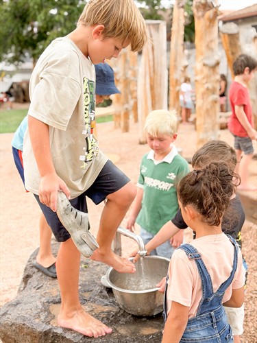 A group a mixed-age learners who are playing outside with the water pump at Acton Academy St. George