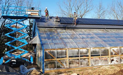 men adding solar panels to the roof of a greenhouse