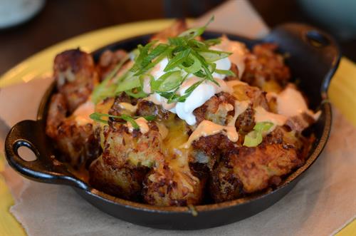 LOADED HOUSEMADE TATER TOTS  PORK CROUTONS, CHEDDAR CHEESE, GREEN ONIONS & SRIRACHA CREAM