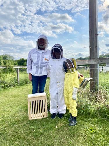 A family dressed in beekeeping suits stands near the bee apiary at Shepard Farm.
