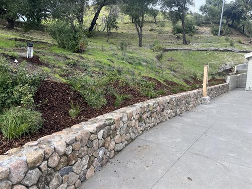 Landscaped yard with rock wall, outdoor shower, outdoor Kitchen and outdoor fireplace