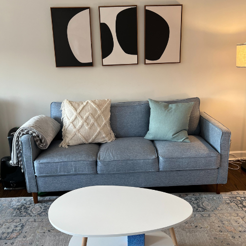 Photo shows a our therapy office with a blue couch, table, and black and white art on the wall