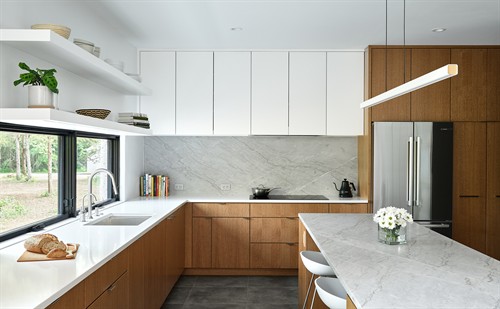 Warm white oak cabinets and bright countertops are balanced by dark earthen tiles to ground the space in this modern kitchen, creating an open, airy space that feels like being outdoors while inside.