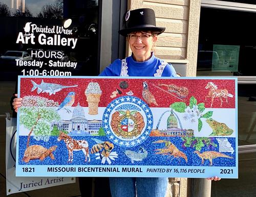 Barb Bailey holding a large replica of the Missouri Bicentennial Mural
