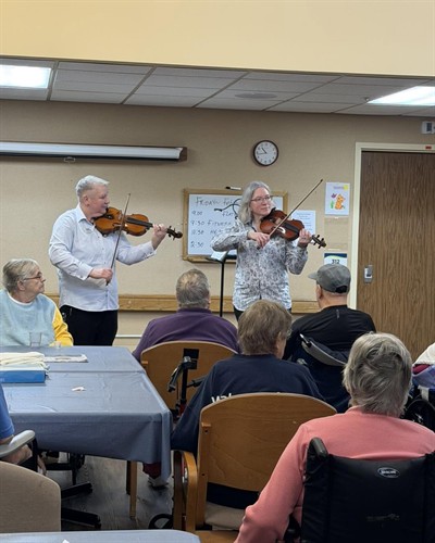 A violin duo plays for Brendan House residents as part of the Logan Health Heartstrings initiative.