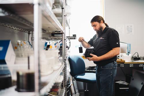 Hands-on inspection: Engineer Jason checking a device in a workspace filled with tools, tech, and supplies.