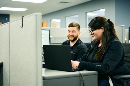 Side-by-side focus: two expert Technicians working on laptops in our modern, well-lit office space.