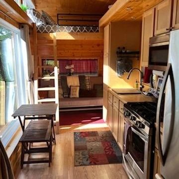 A queen bunk over the living room area that has a smart TV, a futon that makes a 3rd queen bed, and a kitchen with full size stove and fridge.