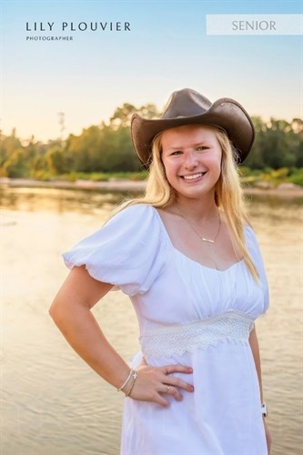 Outdoor portrait in a white dress and wide-brim hat, photographed by the water at golden hour