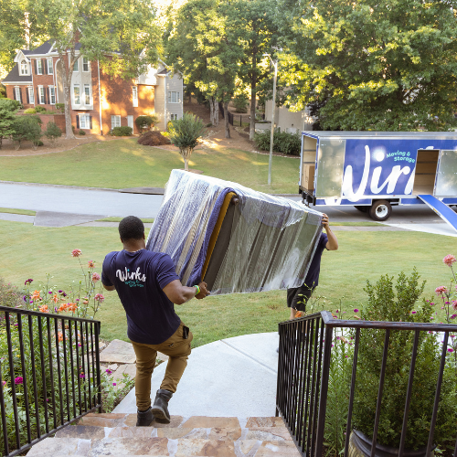 Two professional movers carry a sofa down stairs