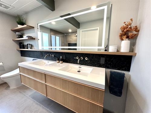 Sleek vanity design with light oak cabinetry, minimalist wall-mounted faucets, and a glowing modern mirror for a clean, spa-like look.