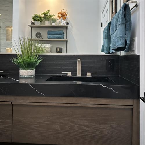 Bold and modern: a bathroom remodel defined by black quartz, sleek flooring, and concrete-inspired walls.