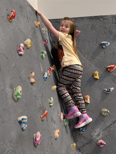 A student building strength and confidence on the indoor climbing wall at Quantum STEM School.