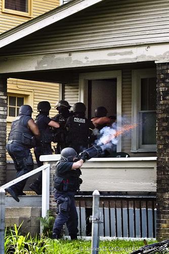 A Columbus Police Narcotics Tactical officer fires a 'knocker' concussion grenade into the front window of a house on East 15th Avenue as the rest of her team makes entry into a drug house.