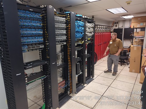 Dale in a MDF server and data room, pointing out a cable. 