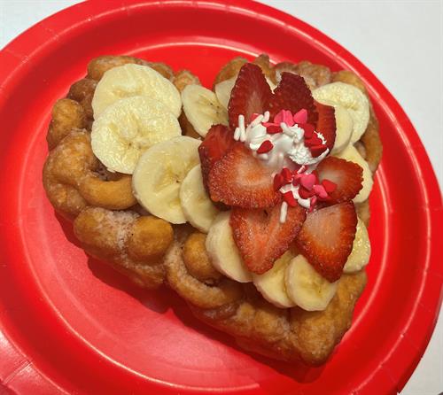 Strawberry & Banana Delight/Funnel Cake with strawberries, bananas, whipped topping, and sprinkles.