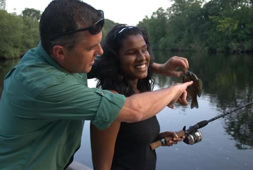 Fishing club is just one component of our summer youth program. A volunteer shows a smiling young woman the fish she just caught. 