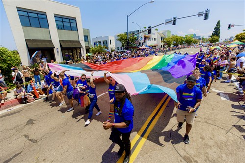 Large pride flag being carried by group of people in a parade