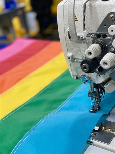 Close up photo of a pride flag laying on a sewing machine being sewn