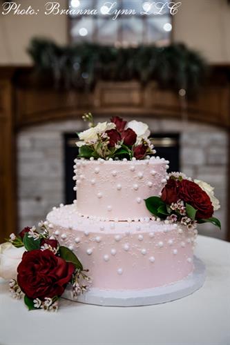 Two-tier cake with pink buttercream and white edible sugar pearls accented with white and red florals