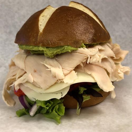 The Wilton : turkey, avocado mash, roasted red peppers, lettuce, onion, & cheese on a pretzel roll 