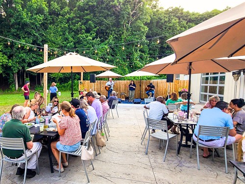 Guests enjoying outdoor dining and live music on Nature's Edge Terrace at Artisanal Brew Works in Saratoga Springs, NY.
