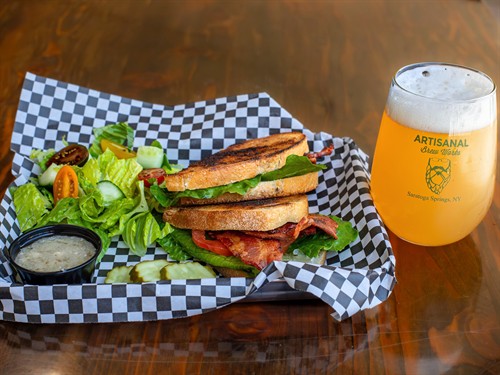 Grilled BLT sandwich served with a fresh side and paired with craft beer at Artisanal Brew Works, a restaurant in Saratoga Springs offering a full menu from Nature’s Edge Bistro and both indoor and outdoor dining on the Nature’s Edge Terrace.