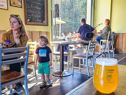 Family enjoying live music and dining at Artisanal Brew Works, a restaurant in Saratoga Springs offering indoor seating and outdoor dining on the Nature’s Edge Terrace.