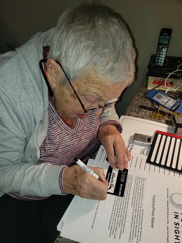 A senior client learning to use a signature guide for signing her name.