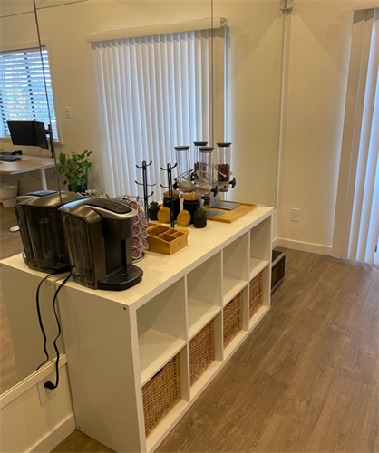 A modern digital marketing office in a Cloverdale corner cleverly doubles as a refreshment station, featuring an espresso machine and toasters, set against a minimalist white shelf unit — the perfect blend of productivity and comfort.