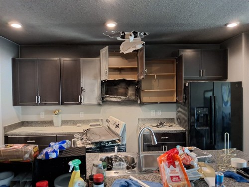 Fire-damaged kitchen area with burned cabinets, damaged drywall, and ceiling damage above the range.