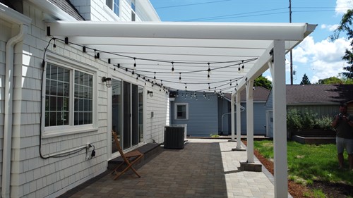 A white pergola with string lighting defines a backyard seating area.