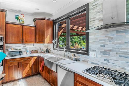 A stunning after-shot of a kitchen remodel in Brighton, MI. New black Soft-Lite picture windows provide an unobstructed view, complemented by a modern tile backsplash and granite countertop. These Energy Star windows drastically update the home's aesthetic.