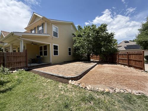 A fresh back yard with a paver patio and decorative rock.