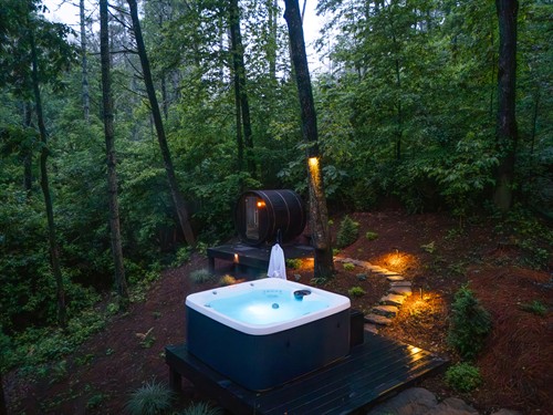 Aerial view of the retreat’s hot tub, firepit, sauna, and upper porch near the Toccoa River. Stone pathways wind between lush mountain laurels, connecting each destination across the terraced landscape.