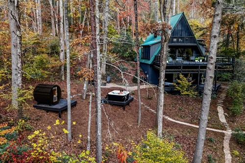 Aerial view of the retreat’s backyard during peak fall color, showcasing a mosaic of gold, crimson, and amber leaves. All exterior amenities—including the sauna, hot tub, firepit, and winding stone pathways—are visible amid the vibrant forest landscape.