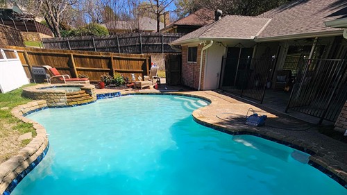 A clean, balanced residential pool featuring a diving board, integrated spa, and an automatic cleaner in action.