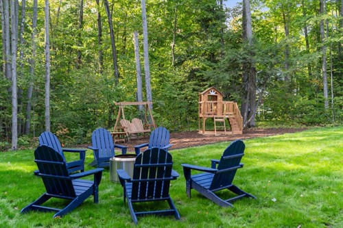 Fire pit with Adirondack chairs; backyard playset just behind