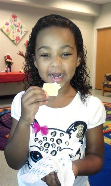 Gabrielle tasting a cracker with butter that she just made at an American Girl Book Club meeting at the Southwest Branch Library