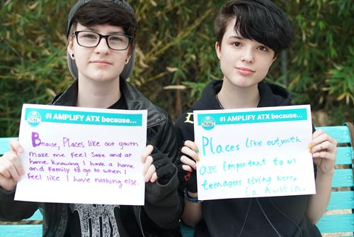 Two young people hold signs for Amplify Austin explaining why Out Youth is important to them.