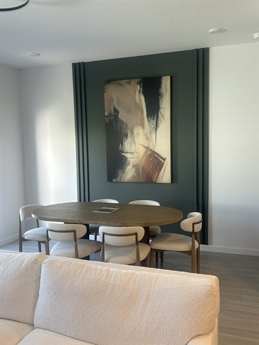 Dining Area with Accent Wall This elegant dining nook pairs warm wood tones with a bold  accent wall, adding depth and drama to the space. The abstract artwork introduces earthy hues and movement, while the oval table and upholstered chairs invite intimate gatherings in a refined, minimalist setting.
