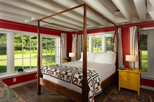 Summer kitchen bedroom is surrounded by windows and the door to the screen porch.