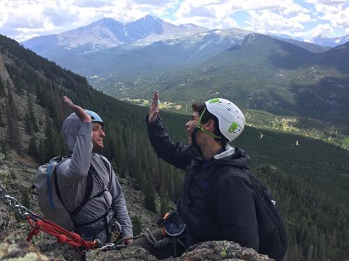 Two rock climbers wearing helmets and ropes high five