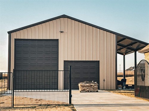 A backyard metal shop with driveway approach, big garage doors, and a lean-to patio on the side.