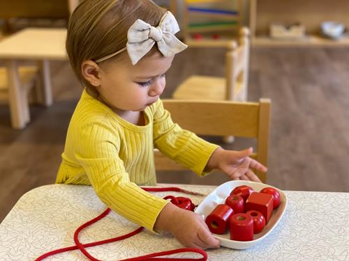 A toddler prepares her bead lesson to work on fine motor skills