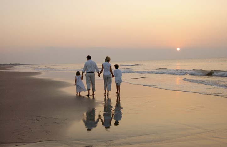 Family of 4 walking on the beach at sunrise on Sunset Beach, NC