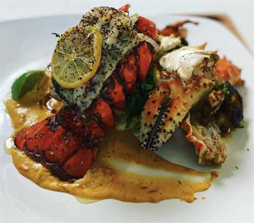 Creole Lobster Tail in Creamy Cajun Sauce over Fried Grit Cakes, Blackened Shrimp, and Poached Crab Legs