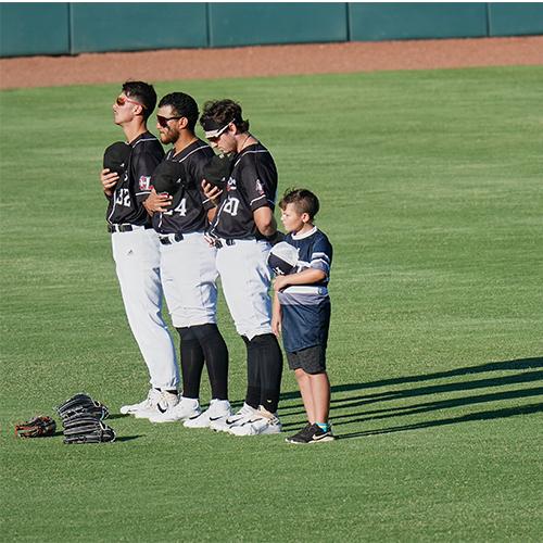 Members of a little league team stand with Crawdads outfielders for the National Anthem