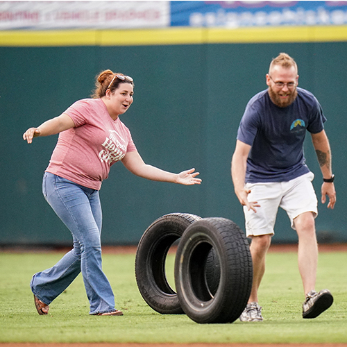 Contestants compete in a tire roll between innings